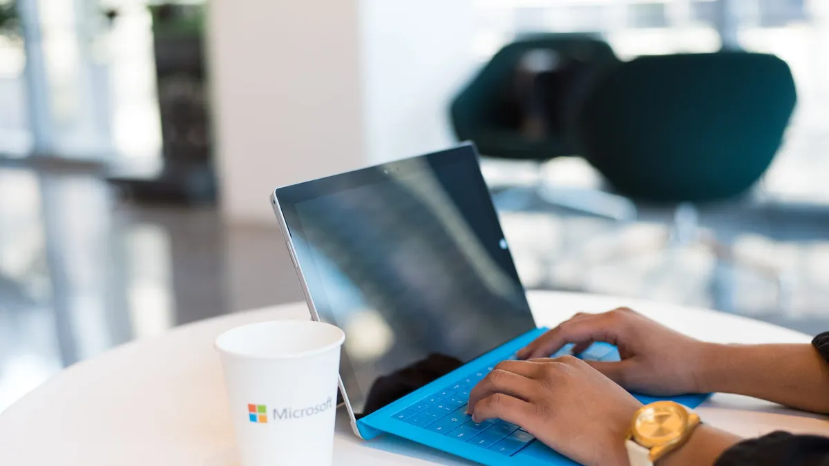 Hands typing on a blue keyboard with a branded cup on a table.