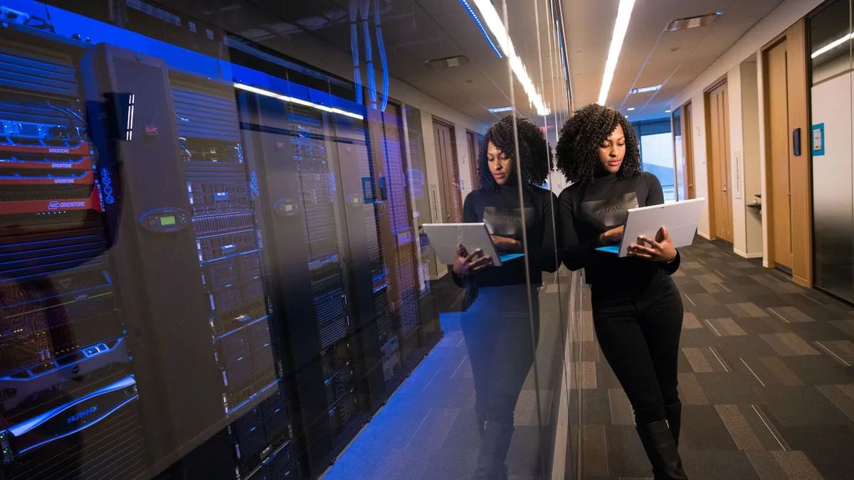 A woman using a laptop navigating a contemporary data center with mirrored servers.