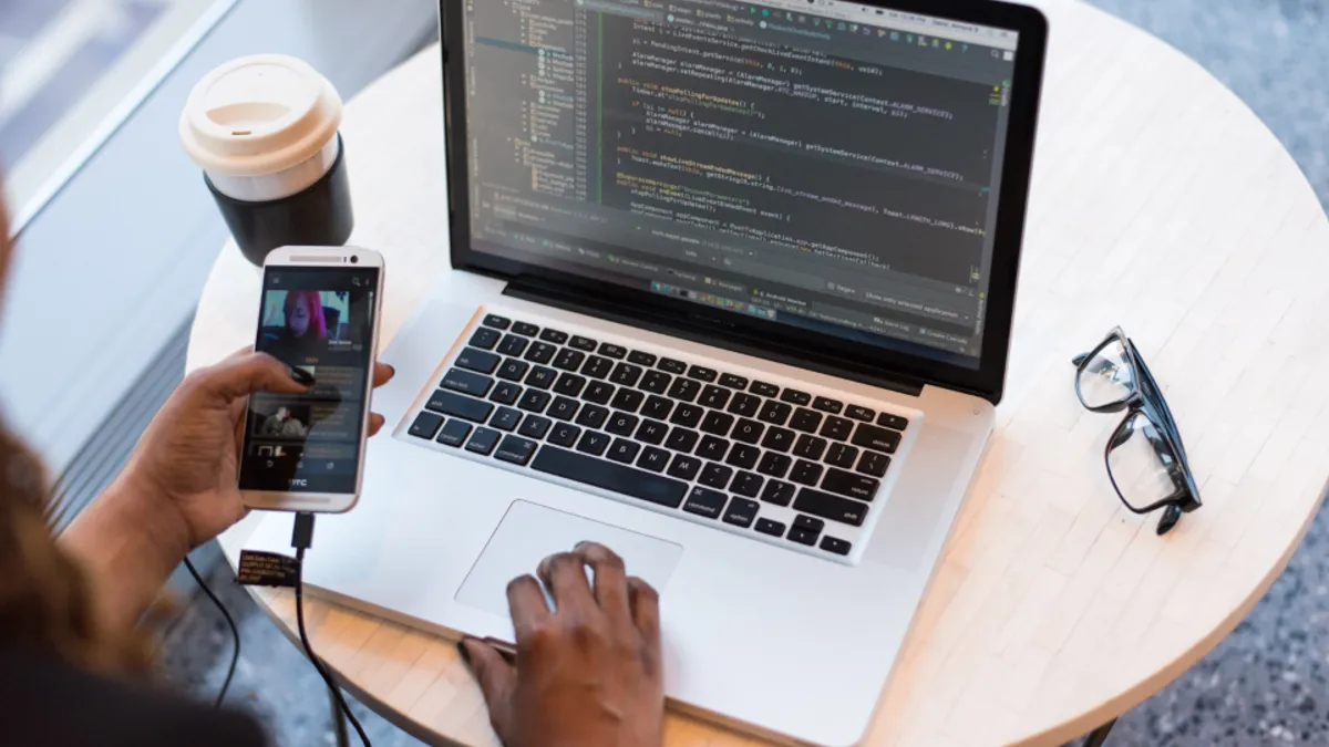 Pessoa trabalhando em um notebook com código na tela e um smartphone na mão