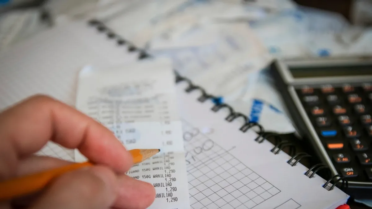 Mão fazendo contas com calculadora e caderno, representando a rotina financeira
